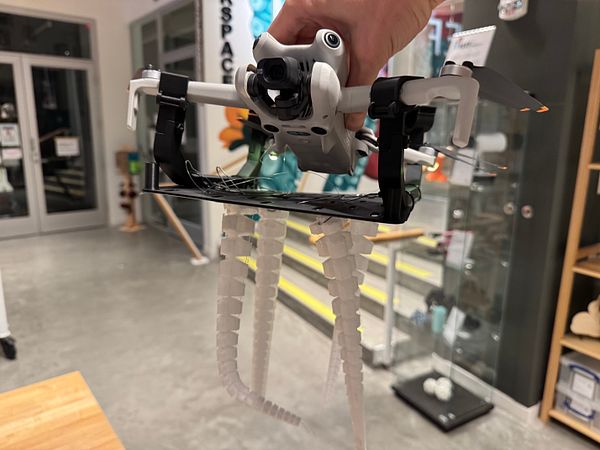 A drone equipped with tentacle-like appendages is being held in a workspace.