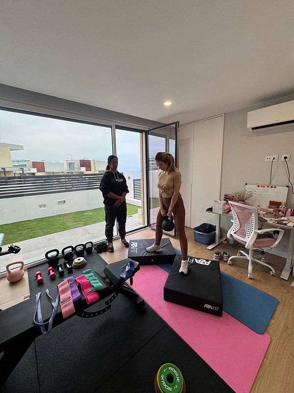 A home gym setup in a small room features two women engaged in a workout session.