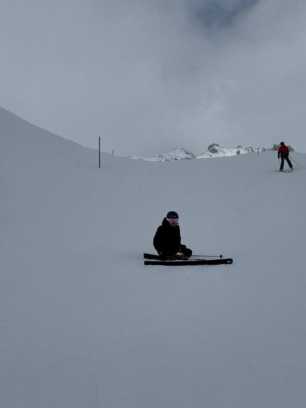 A person is sitting on a ski slope, surrounded by snow and mountains.