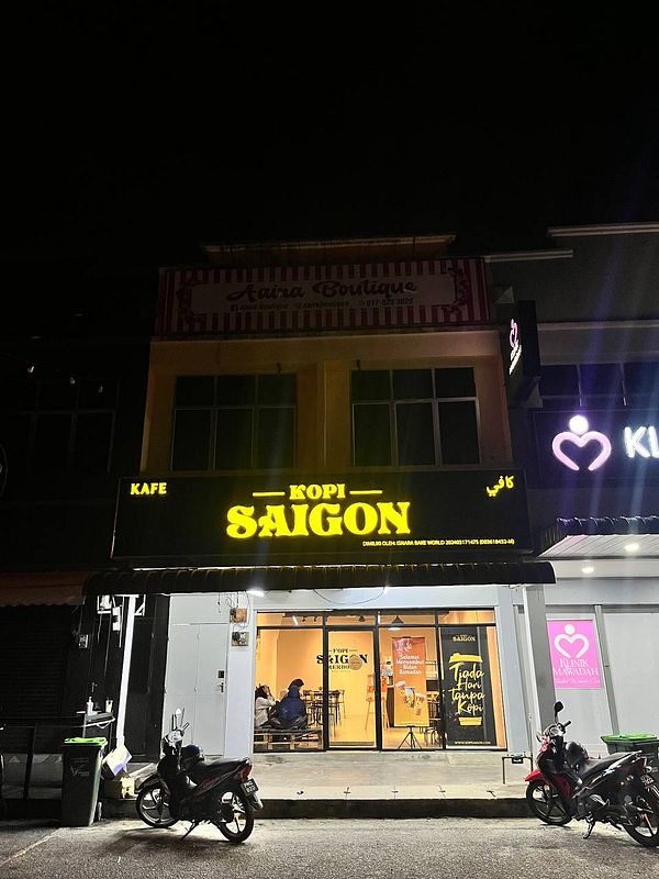 A brightly lit café named 'Kopi Saigon' is visible at night, showcasing its inviting exterior.