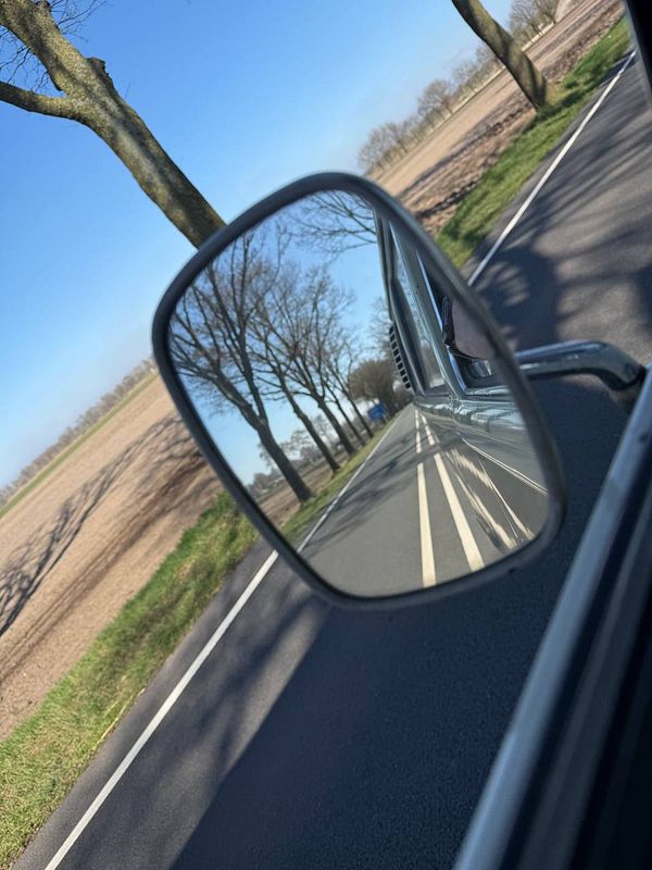 Smiling man in overalls repairs a bicycle tire in a workshop filled with tools.