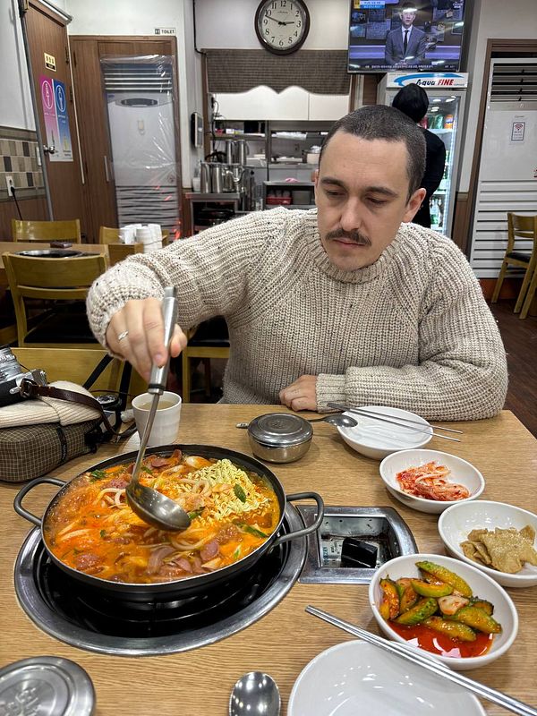 A man is enjoying a bowl of 부대찌개 in a cozy restaurant setting.