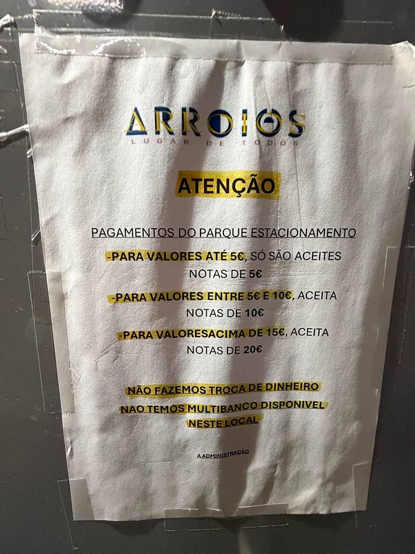 A parking machine in Lisbon with a paper note explaining payment instructions, including the preference for €5 coins or bills, alongside a partially visible wallet and some cash.