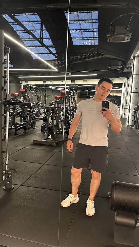 A person is taking a selfie in a gym setting, showcasing fitness equipment in the background.