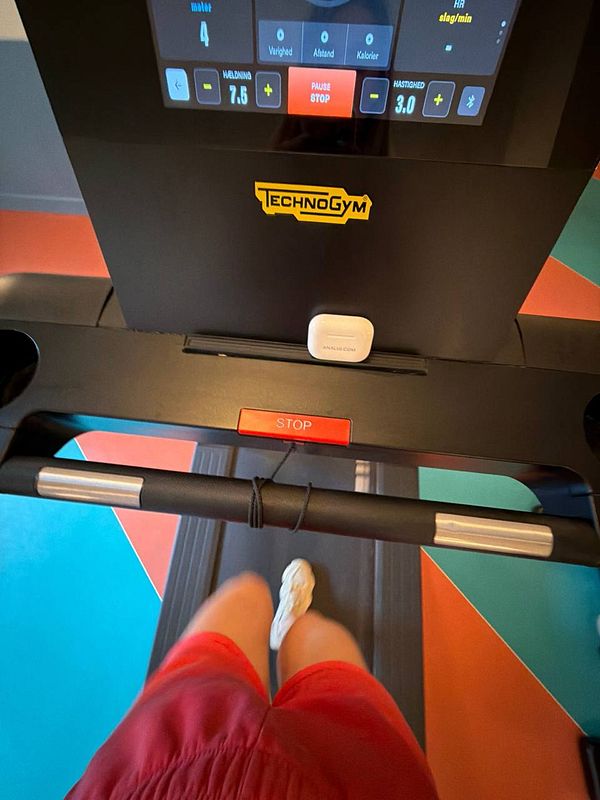 A low-angle photo taken inside a gym showing a person in a white hoodie working out on a punching bag with boxing gloves.
