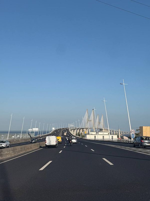 A scenic view of a highway leading towards a modern bridge in Portugal under a clear blue sky.