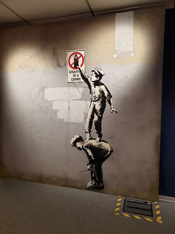 A Banksy artwork depicting two children interacting with a 'Graffiti is a crime' sign.