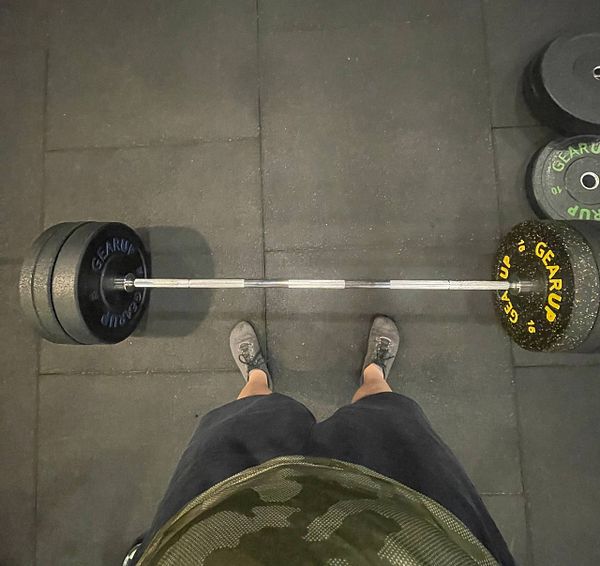 A person stands over a barbell loaded with weights in a gym setting.