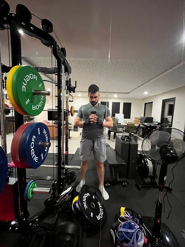 A man is taking a selfie in a gym setting, surrounded by workout equipment.
