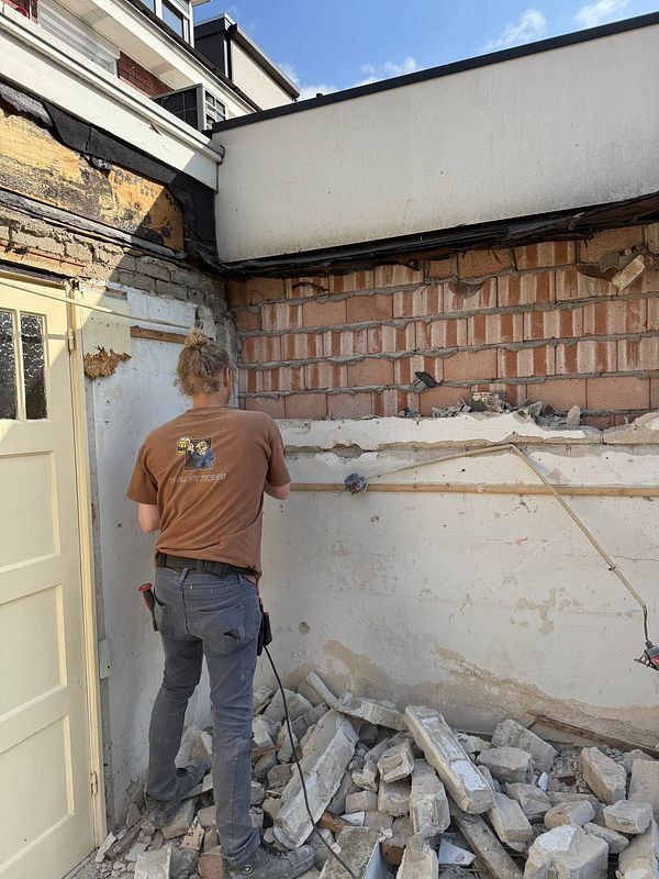 A person is actively engaged in demolition work on a wall, surrounded by debris.