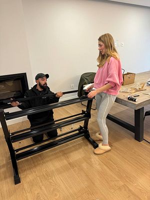 A man and a woman are assembling gym equipment in a spacious room.