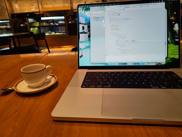 A workspace setup featuring a laptop, a cup of coffee, and a wooden table in a café.