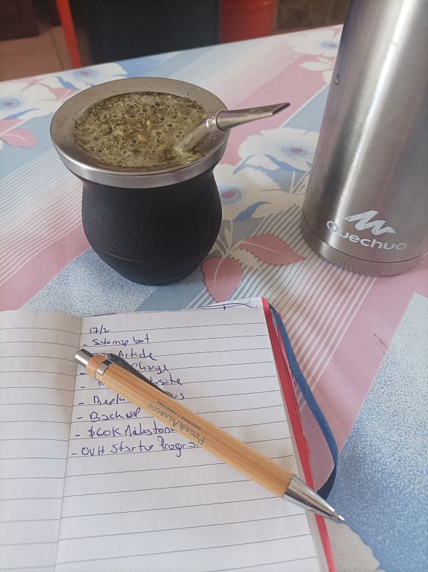 A cozy workspace featuring a traditional mate drink, a notebook with tasks, and a thermos.