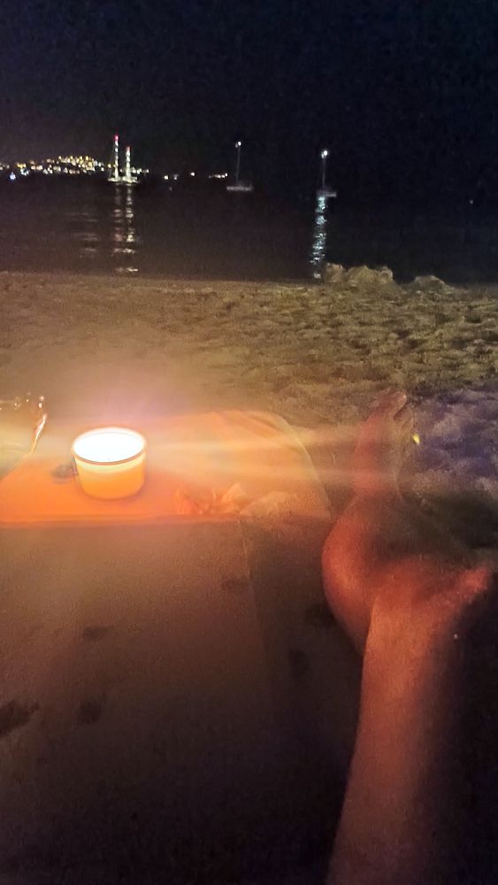 A serene beach scene at night featuring a candle and a person's feet in the sand.