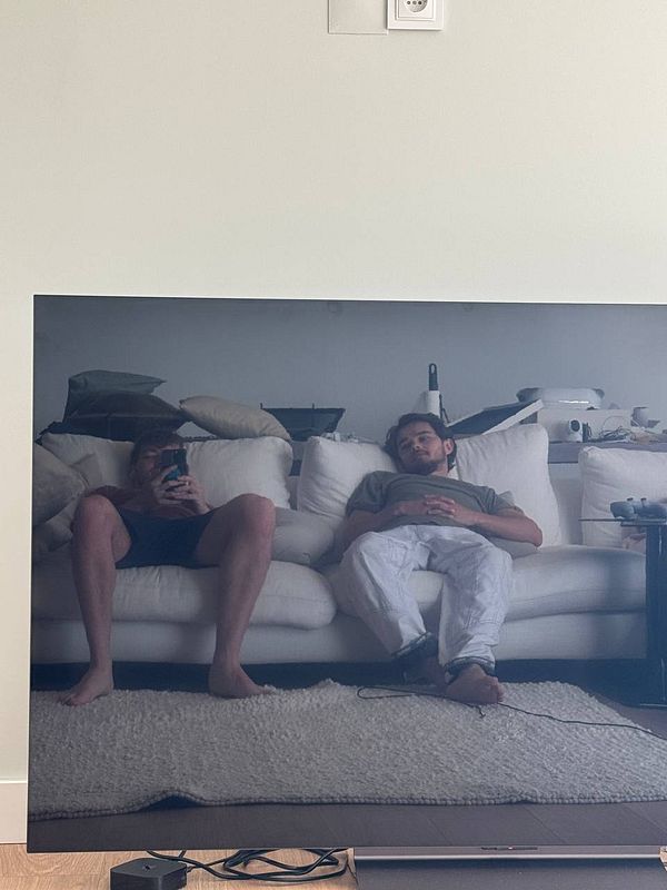 Two individuals are lounging on a couch, reflected in a large screen.