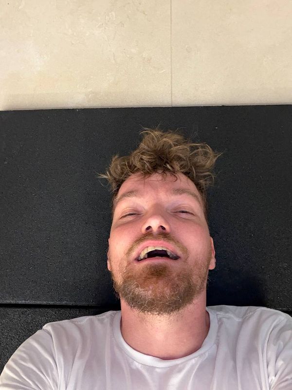 An athletic woman in a gym environment is seated on a workout bench with a kettlebell in one hand, wearing fitness apparel.