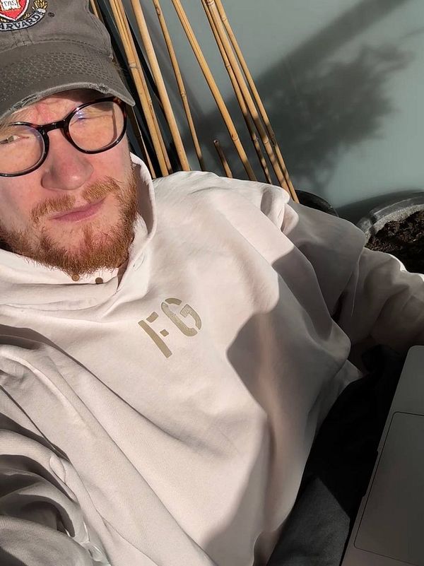 A small round table on a sunny balcony with a laptop, headphones, a glass of iced tea, and a tube of lip balm in a cozy outdoor setting.