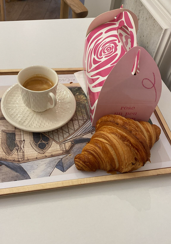 A cozy coffee setup featuring a cup of espresso, a croissant, and a decorative takeout box.