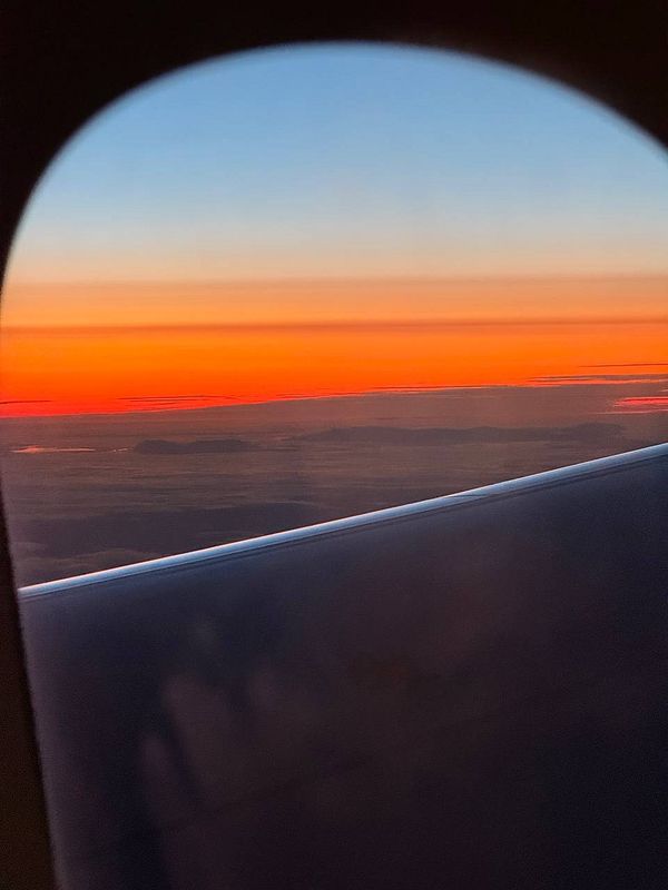 A vibrant sunset view from an airplane window, showcasing a gradient of colors in the sky.