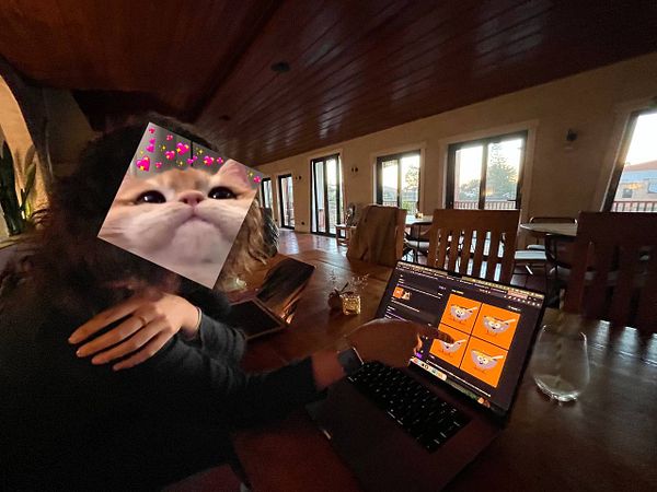 A person is sitting at a cafe table, working on a laptop while pointing at the screen.