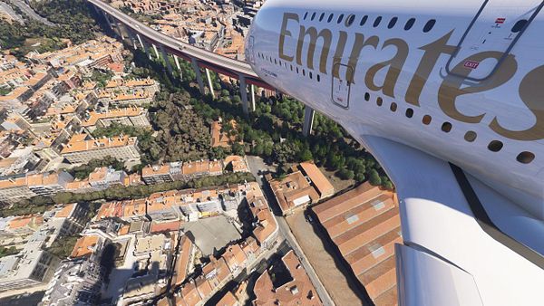 An Emirates A380 aircraft is flying over a densely populated area of Lisbon, showcasing the cityscape below.
