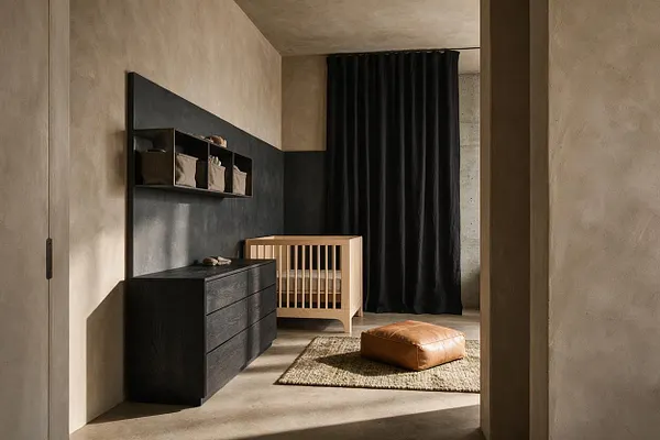 A minimalist nursery with a light wood crib, matte black dresser, and dark wall-mounted shelving with fabric storage bins. The room features textured beige walls, a concrete-like floor, a black curtain, a woven rug, and a tan leather floor cushion, creating a warm Brutalist atmosphere.