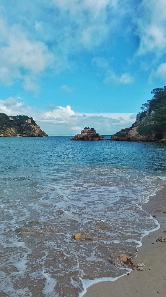 A couple walking hand in hand on a grassy hillside surrounded by rocky terrain under a partly cloudy sky.