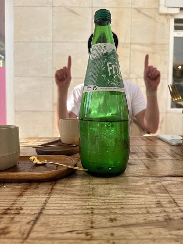 A woman sitting on a wooden bench in a natural grassy area eating food from a pink container.