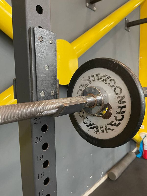 A close-up view of a barbell resting on a squat rack in a gym setting.