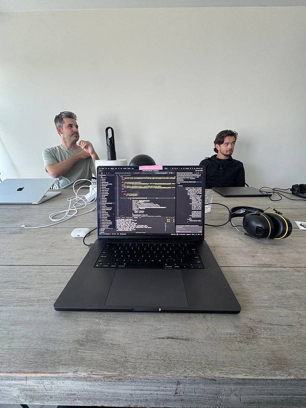 A coworking space setup featuring a laptop with code on the screen and two individuals in the background.