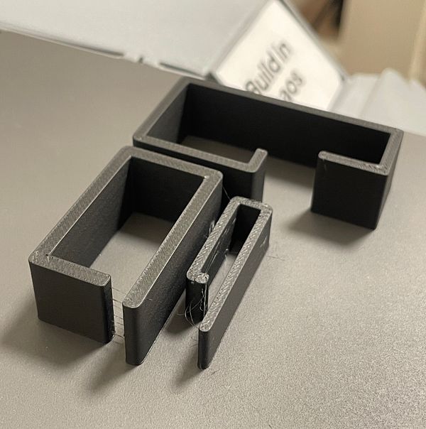 Three custom 3D printed U-clips on a laptop stand holding a hub, cable and video capture device.