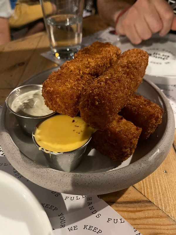 A plate of crispy mac and cheese sticks served with dipping sauces.