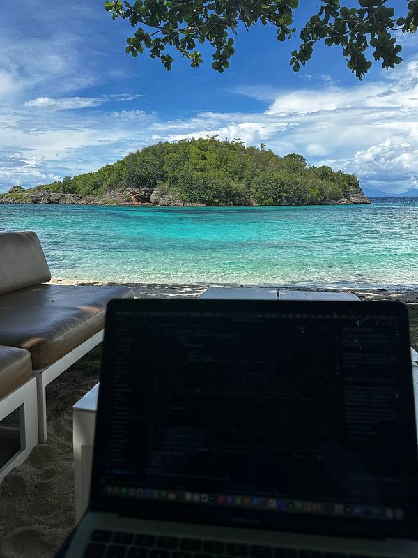 A serene beach scene with a laptop in the foreground and a lush island in the background.