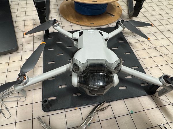 A drone is positioned on a black baseplate in a makerspace environment.