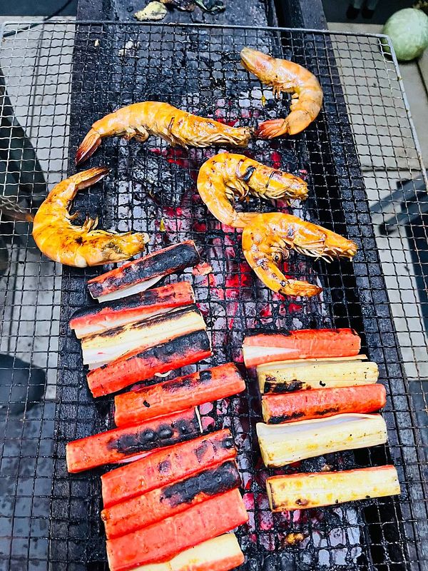 Grilled shrimp and vegetables are being cooked on a barbecue grill.