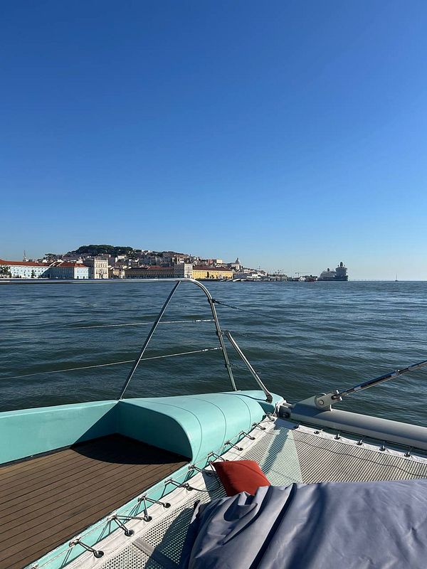 A scenic view from a catamaran showing the Lisbon waterfront under a clear blue sky.