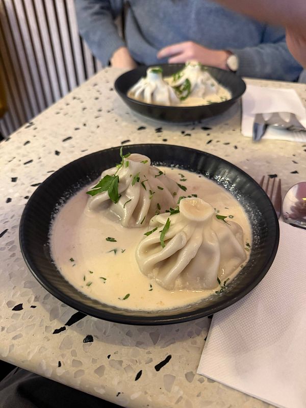 A table setting featuring Georgian cuisine including breads, nuts, herbs, and cheeses with a pitcher and glasses on a wooden table.