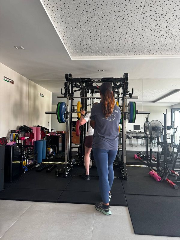 A personal trainer assists a client with weightlifting in a modern gym setting.