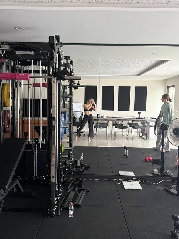 Photograph of a person standing in a gym parking lot next to a sports car at sunset with a city skyline and water in the background.