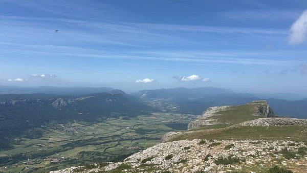 Scenic mountain hike trail with hikers overlooking green valleys and rocky peaks under a blue sky with clouds.