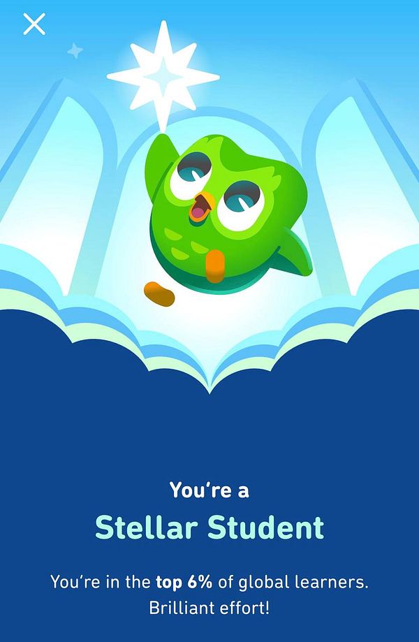A cheerful green owl character celebrates a user's achievement in language learning.