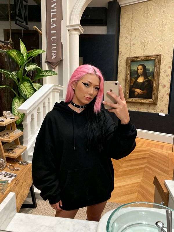 A young woman with pink hair poses for a selfie in a stylish interior featuring art and decor.