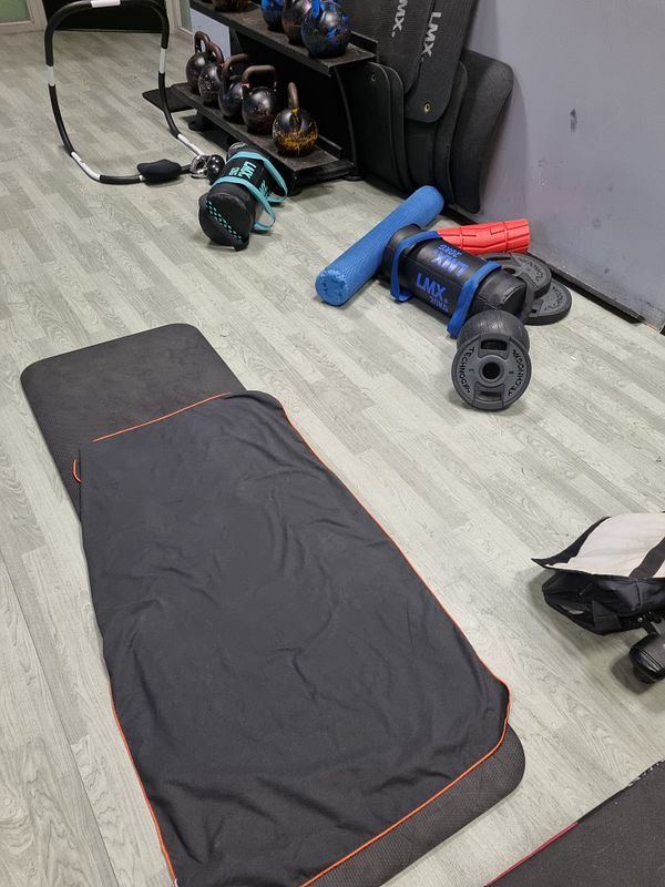 The image depicts a gym area with various strength training equipment and a workout mat.