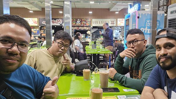 A group of four friends is enjoying a casual meetup at a vibrant food court.