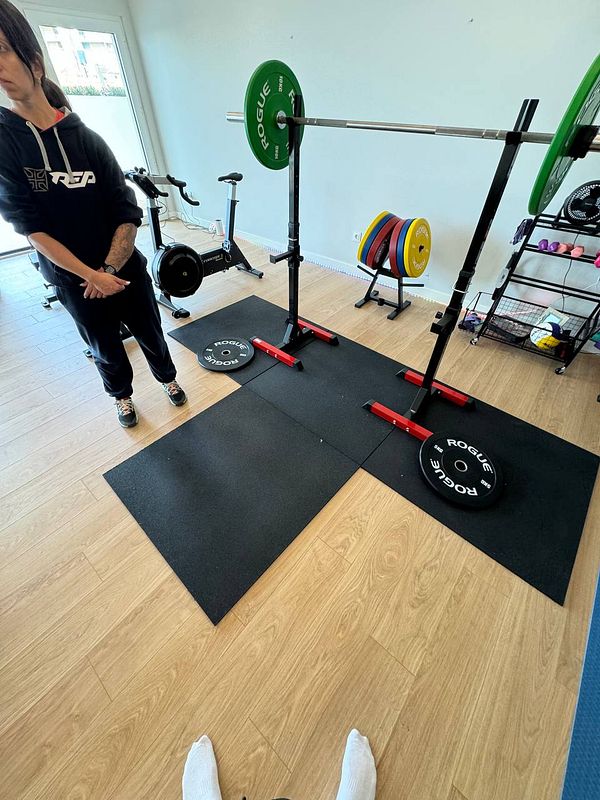 A home gym setup featuring weightlifting equipment and a personal trainer.