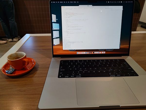 A laptop displaying code sits on a wooden table next to an empty coffee cup.