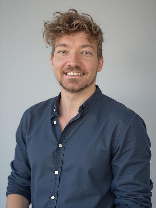 A smiling man with curly hair poses for a headshot against a neutral background.