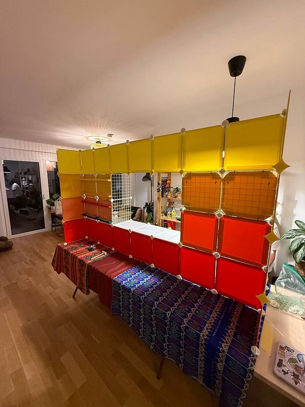 Top-down photo of a large rectangular wooden booth frame with a cardboard roof panel in an indoor workspace.