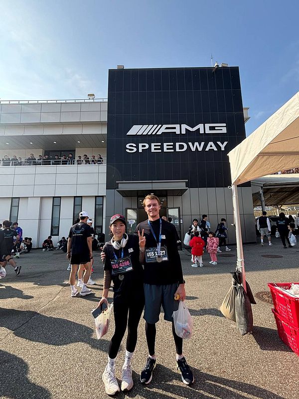Two participants pose in front of the AMG Speedway after completing a 10k race.
