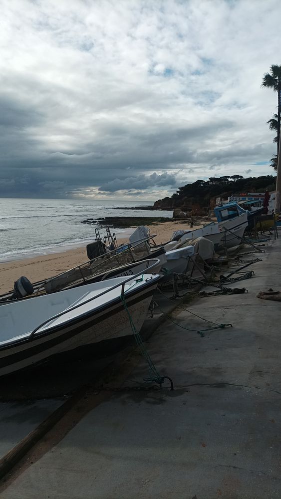 A scenic view of fishing boats lined up on a sandy beach with a cloudy sky overhead.